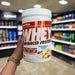 Close-up of (PER4M Whey Protein Powder 900g) held up inside My Supplement Shop, clearly showing the front label in a Sports Nutrition setting.